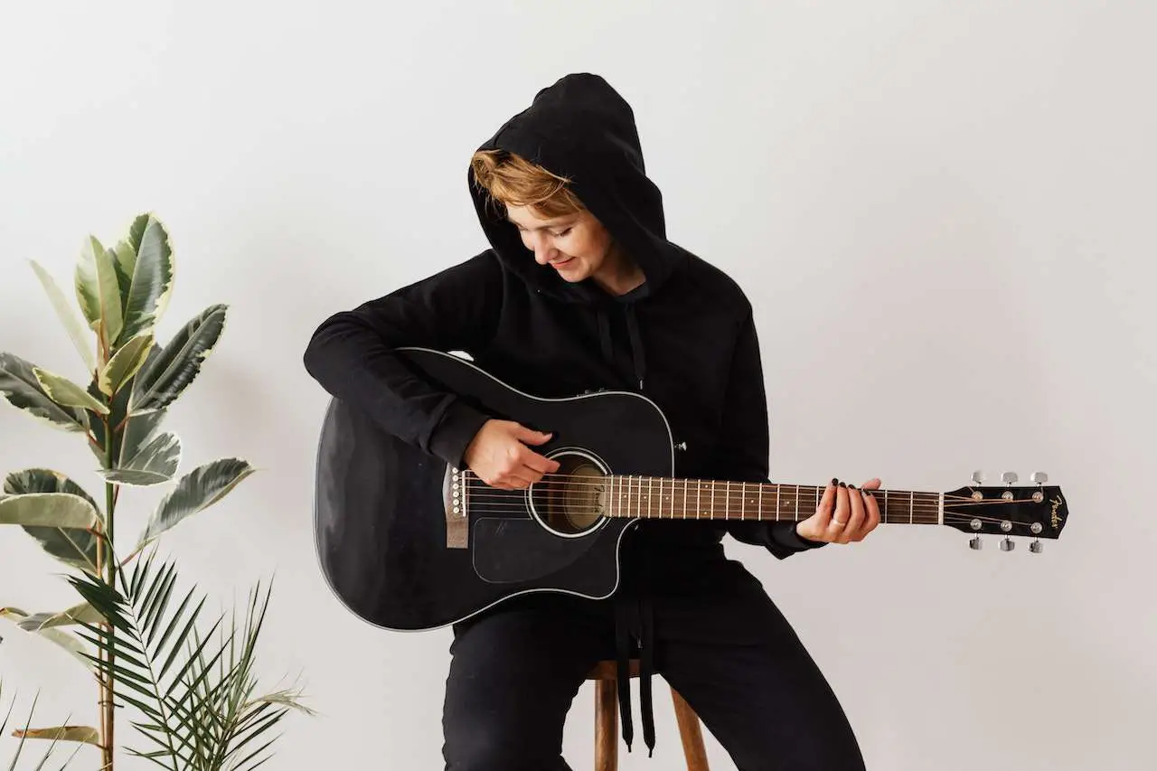 girl in hoodie practicing her acoustic guitar
