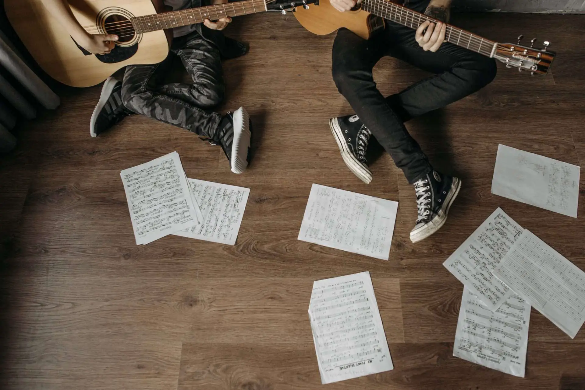 2 guitar players sitting on floor with sheet music surrounding them