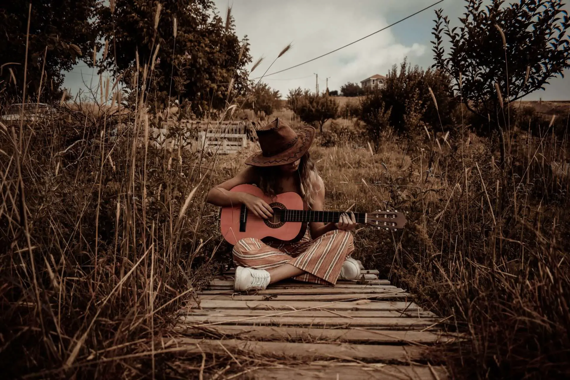 a girl sitting down near a dock and playing her guitar