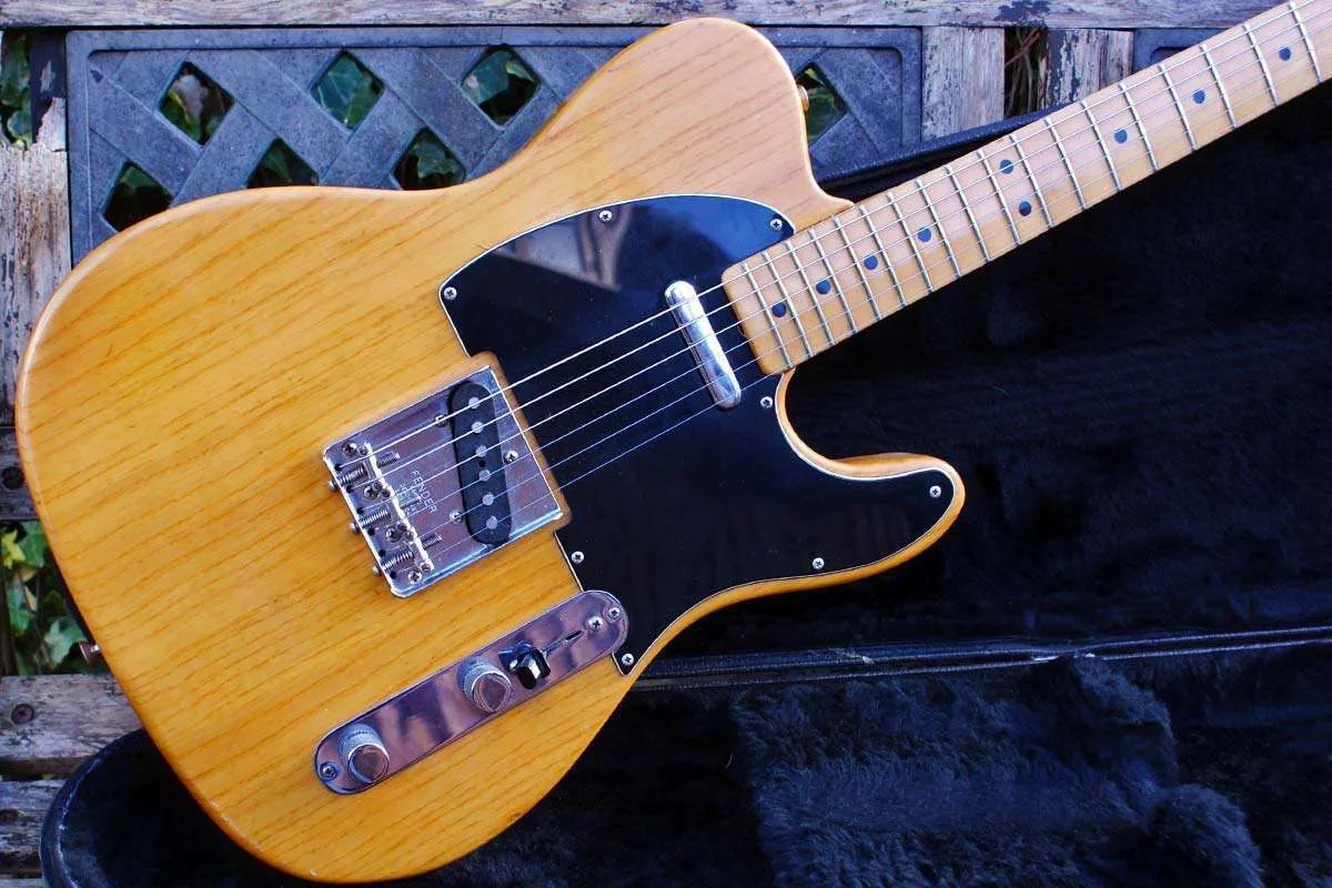 Dimensions of a Telecaster Body, 16 inches wide, 12.75 inches long, and 1.75 inches thick, with a distinct waist and rounded edges, sits on a workbench