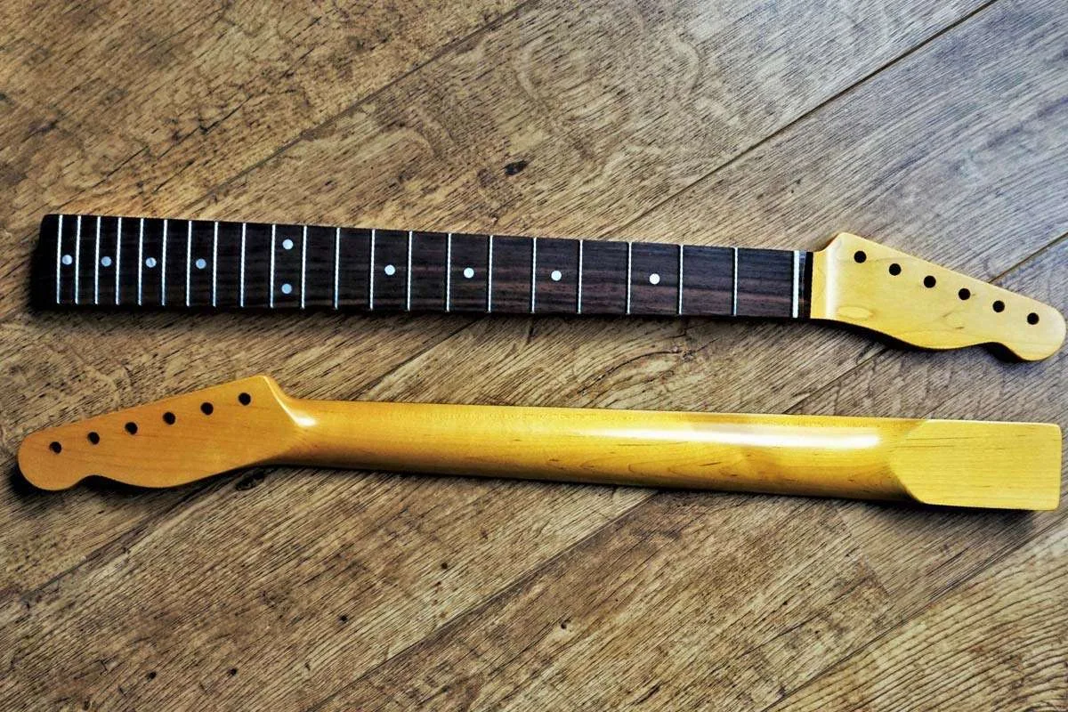 two telecaster necks without a tele body laying on a wooden floor for comparison